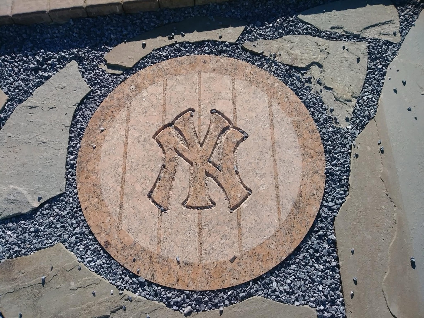 New York Yankees NY logo inlay carved in tan stone, set into a flagstone patio with a gravel border