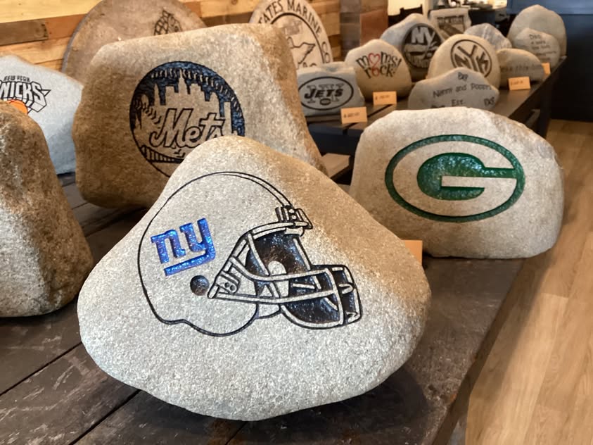 Display of engraved rocks including Mets, Giants, and Green Bay Packers logos