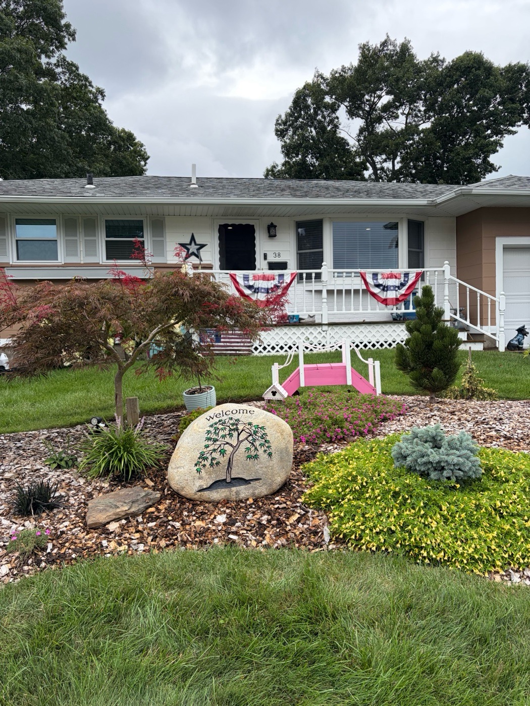 Welcome engraved rock with a tree design, set in a front yard garden bed