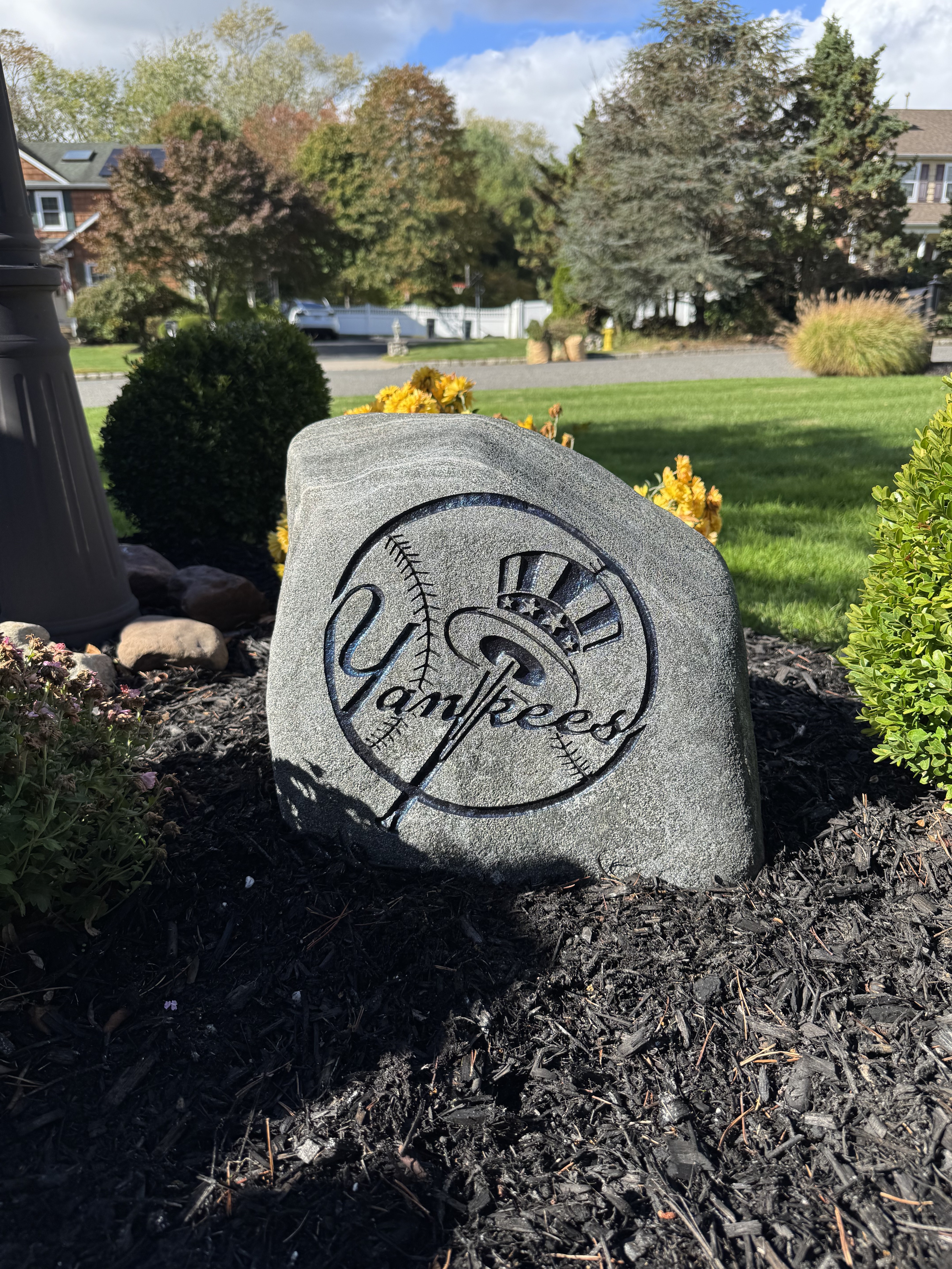 New York Yankees top hat logo engraved rock in a garden bed